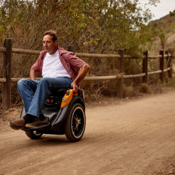 A man on an orange Omeo rides along a dirt path.